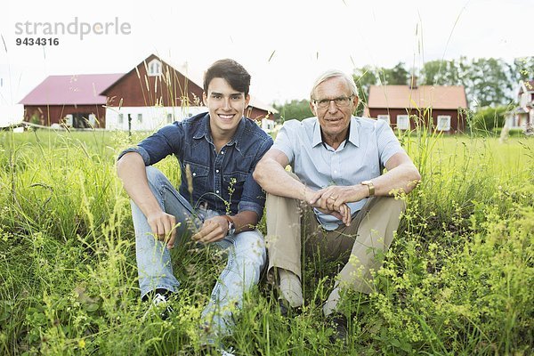 Portrait von Großvater und Enkel auf einem grasbewachsenen Feld sitzend