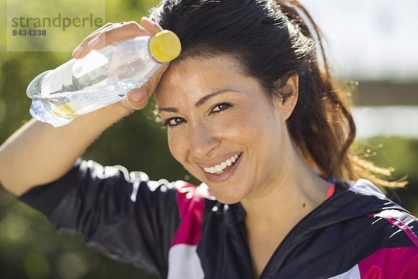 Porträt einer fröhlichen Frau  die den Schweiß wischt  während sie die Wasserflasche in der Hand hält.