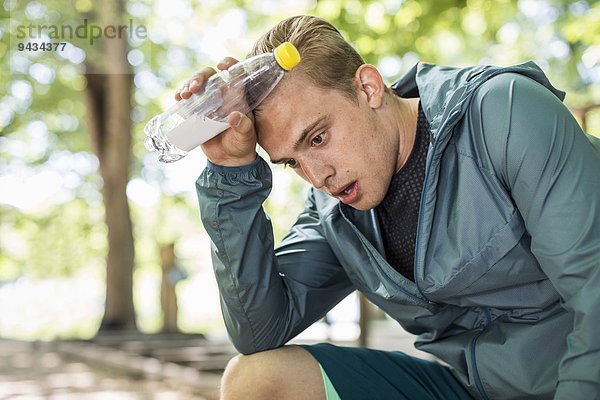 Müder Mann keucht  während er nach dem Training im Park die Wasserflasche hält.
