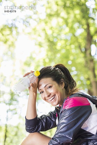 Porträt einer fröhlichen Frau mit Wasserflasche im Park