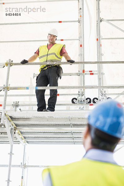 Rückansicht des Architekten mit Blick auf den am Geländer stehenden Bauarbeiter