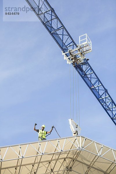 Niederwinkelansicht des erfolgreichen Arbeiters auf dem Dach auf der Baustelle