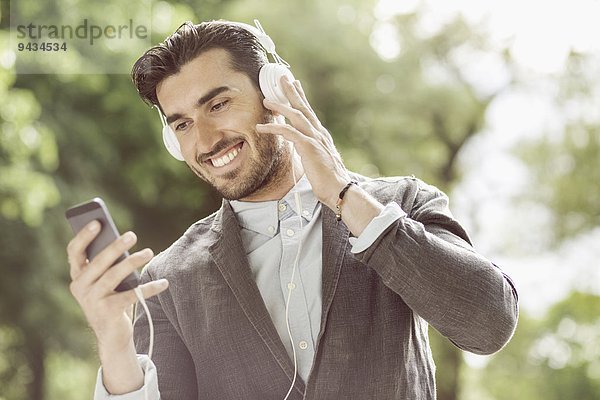 Glücklicher Geschäftsmann  der Musik über ein Smartphone im Freien hört.