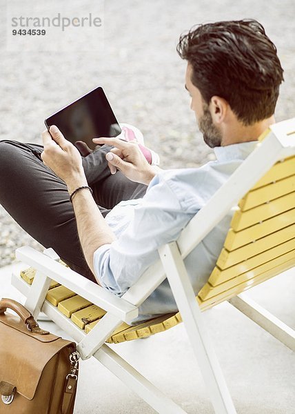 Rückansicht des Geschäftsmannes mit digitalem Tablett auf Lounge Chair im Park