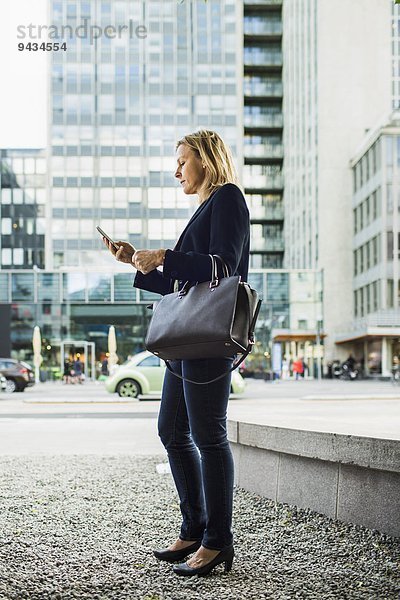 Durchgehende Seitenansicht der Geschäftsfrau mit dem Handy auf dem Bürgersteig der Stadt
