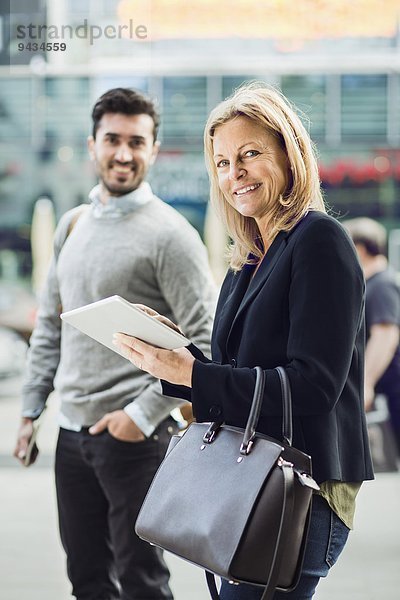 Portrait einer Geschäftsfrau mit digitalem Tablett auf der Stadtstraße mit Kollegin im Hintergrund
