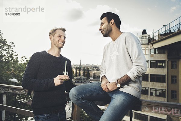 Glückliche männliche Freunde kommunizieren auf dem Dachgarten