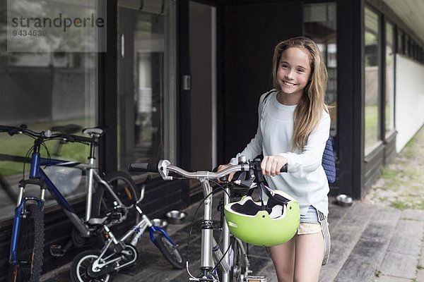 Fröhliches Mädchen beim Spaziergang mit dem Fahrrad vor dem Haus