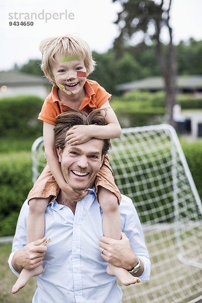 Porträt eines glücklichen Vaters  der einen verletzten Jungen auf den Schultern trägt.