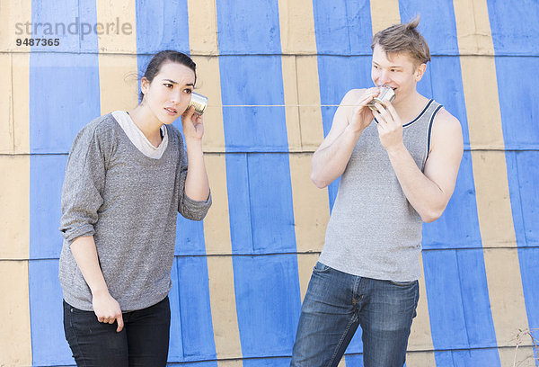 Junger Mann spricht in eine Blechdose hinein und eine junge Frau hört zu  Dosentelefon  Symbolbild  Kommunikation in einer Beziehung