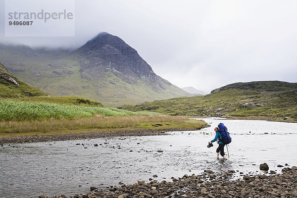 Frau mit Rucksack durchquert den Fluss Abhainn Camas Fhionnairigh  hinten Sgurr Hain  Camasunary  Isle of Skye  Schottland  Großbritannien  Europa