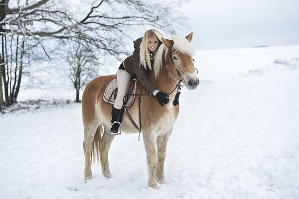 Junge Frau reitet auf einem Haflinger im Schnee