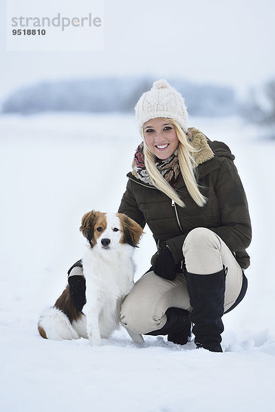 Junge Frau mit einem Kooikerhondje-Hund im Schnee