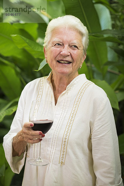 Porträt einer lächelnden Seniorin mit einem Glas Rotwein