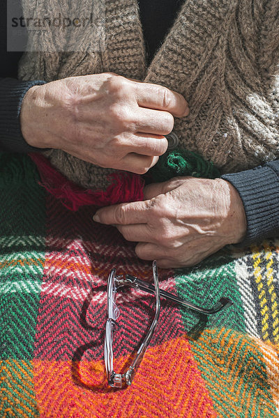 Hände einer älteren Frau  die ihre Weste zuknöpft  während die Brille auf der Decke liegt.