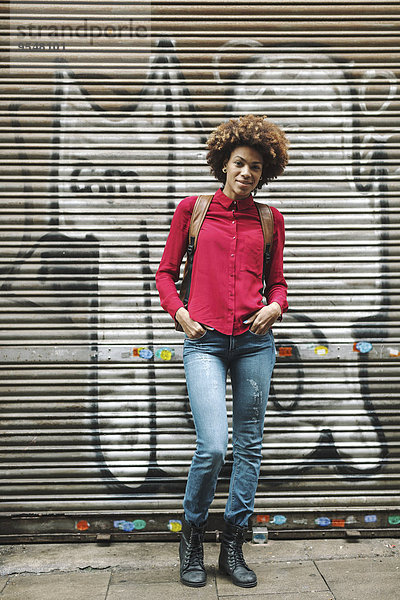 Lächelnde junge Frau steht vor dem Rollladen mit Graffiti