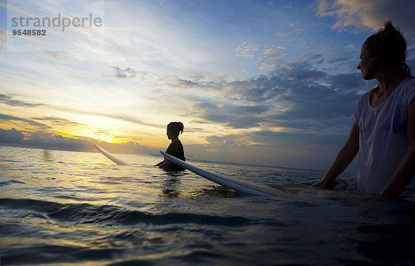 Indonesien  Bali  Canggu  zwei Surferinnen im Wasser  die die Sonne beobachten.