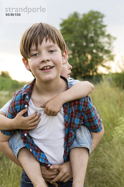 Porträt eines lächelnden kleinen Jungen  der seinem Bruder Huckepack gibt.