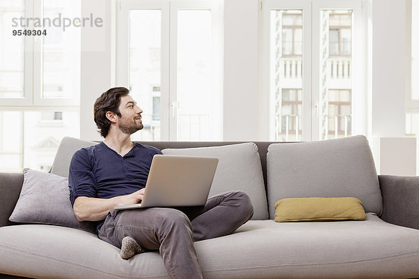 Mann auf der Couch sitzend mit Laptop