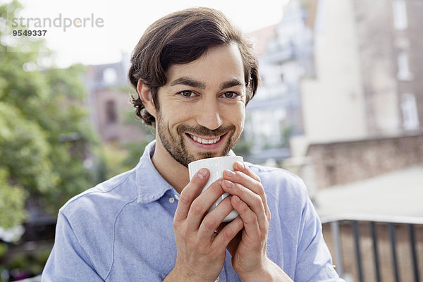 Porträt eines lächelnden Mannes auf dem Balkon beim Kaffeetrinken