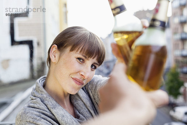 Lächelnde Frau auf dem Balkon klirrende Bierflasche