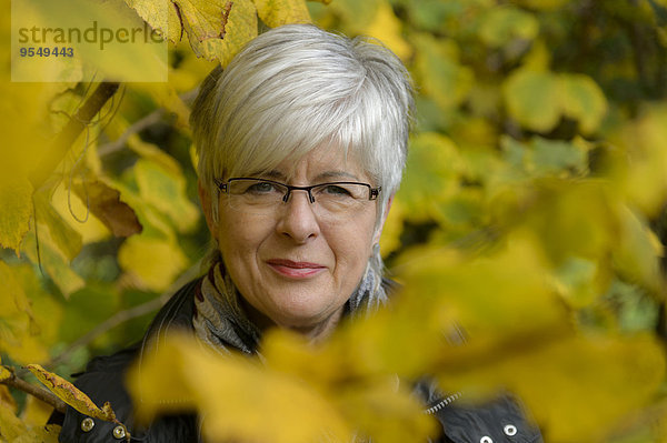 Porträt einer lächelnden Seniorin mit kurzen grauen Haaren und Brille