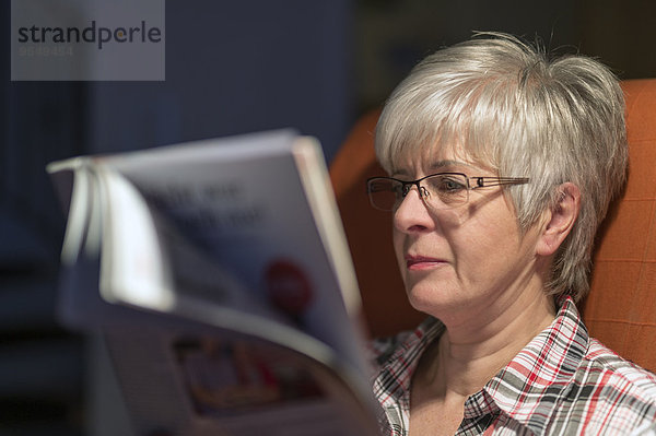 Seniorin beim Lesen der Zeitschrift am Abend