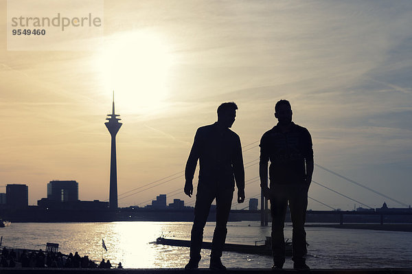 Deutschland  Nordrhein-Westfalen  Düsseldorf  zwei Mann mit Blick auf Rheinturm und Rhein bei Sonnenuntergang