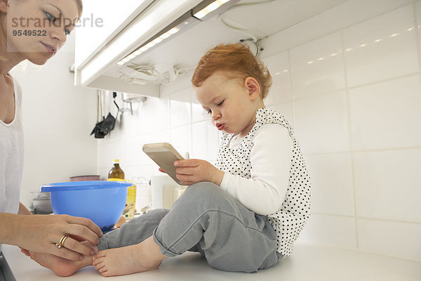 Kleines Mädchen sitzend auf der Küchenzeile mit Smartphone