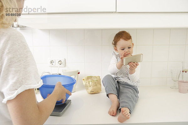 Kleines Mädchen sitzend auf der Küchenzeile mit Smartphone