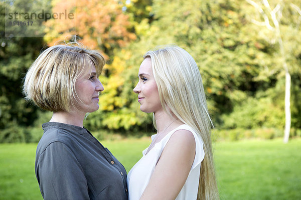 Lächelnde Mutter und erwachsene Tochter im Park stehen sich gegenüber.