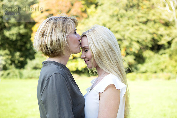 Mutter küsst erwachsene Tochter im Park