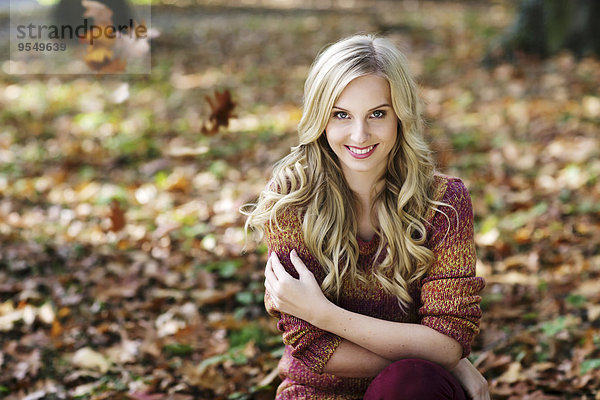 Porträt einer lächelnden blonden Frau mit Strickpullover im Herbstwald