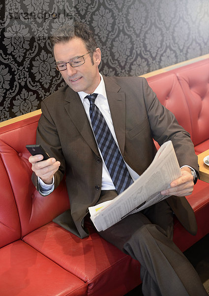Geschäftsmann sitzt in einem Café mit Zeitung mit Smartphone