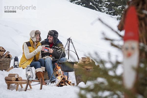 Lächelndes Paar im Schnee am Lagerfeuer
