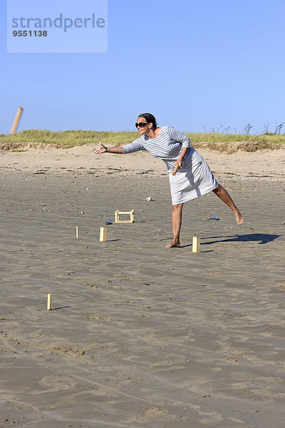 Frau spielt Kubb am Strand