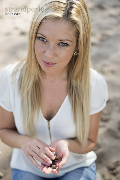 Porträt einer jungen Frau am Strand  die Muscheln in den Händen hält.
