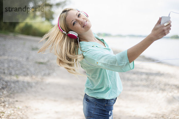 Junge Frau mit Kopfhörer tanzt am Strand