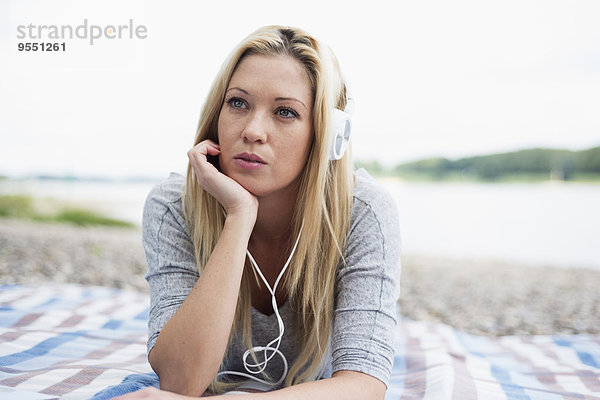 Junge Frau mit Kopfhörer auf einer Decke am Strand liegend