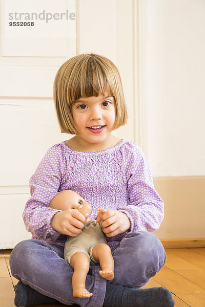 Porträt eines lächelnden kleinen Mädchens  das mit einer Puppe spielt.
