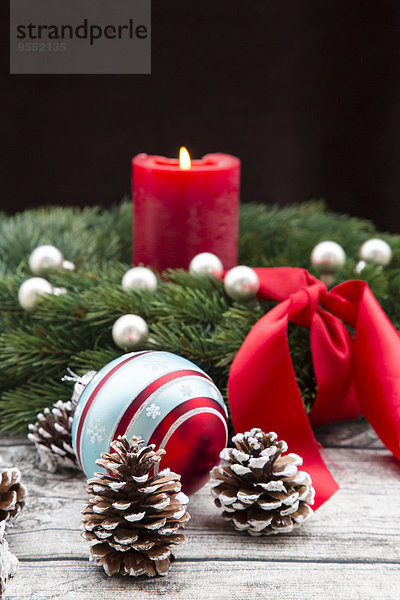 Adventskranz mit angezündeter roter Kerze  Weihnachtskugel und Tannenzapfen auf Holz