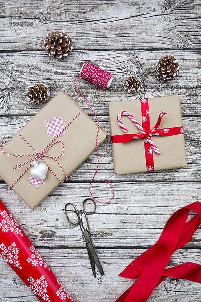 Verpackte Weihnachtsgeschenke  Tannenzapfen  Band und Schere auf Holz