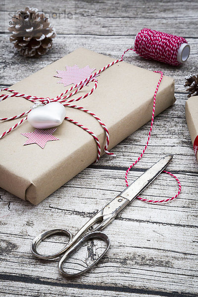 Verpackte Weihnachtsgeschenke  Scheren  Bänder und Tannenzapfen auf Holz