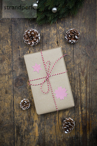 Verpacktes Weihnachtsgeschenk und Tannenzapfen auf dunklem Holz