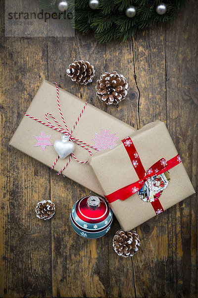 Verpackte Weihnachtsgeschenke  Weihnachtskugel und Tannenzapfen auf dunklem Holz
