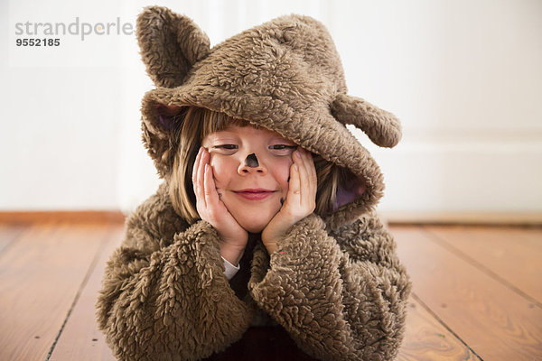 Porträt eines fröhlichen kleinen Mädchens als Bär auf Holzboden liegend