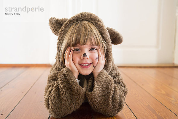 Porträt eines fröhlichen kleinen Mädchens als Bär auf Holzboden liegend