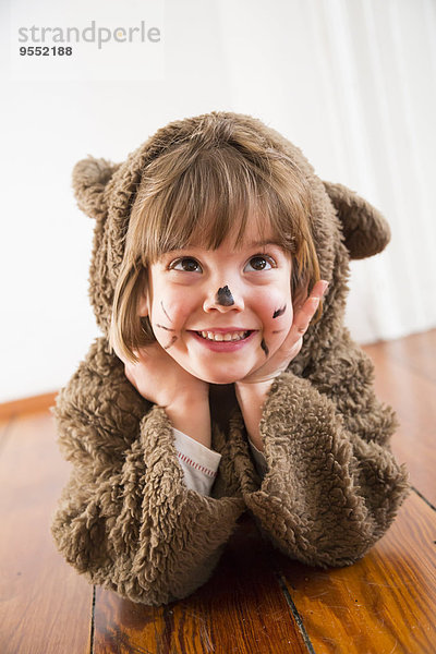 Porträt eines lächelnden kleinen Mädchens als Bär auf Holzboden liegend