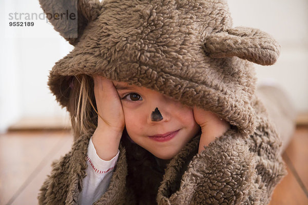 Porträt eines lächelnden kleinen Mädchens als Bär auf Holzboden liegend