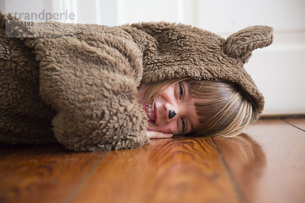 Porträt eines lachenden kleinen Mädchens als Bär auf Holzboden liegend